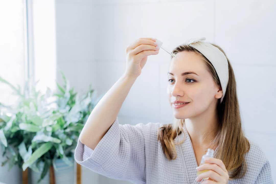 Mujer joven aplicando con un gotero ácido hialuorónico para la cara